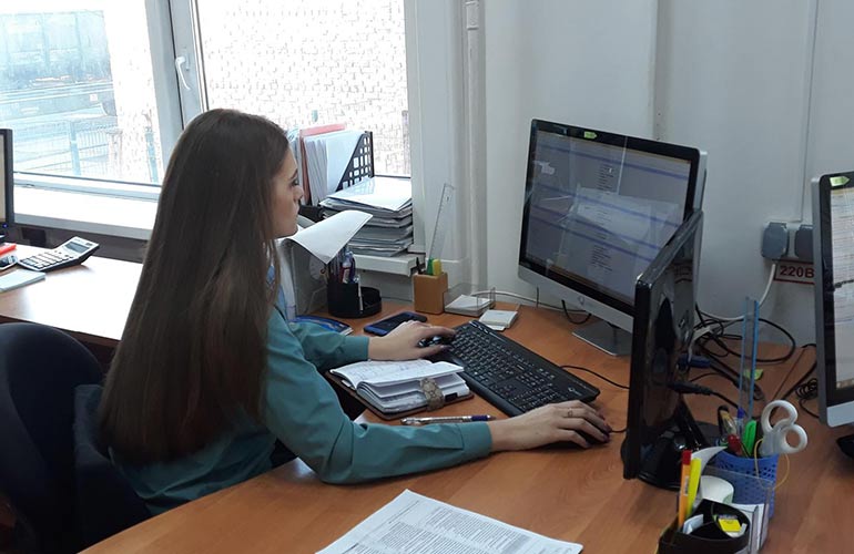 девушка таможенник работает с документами за компьютером, обрабатывая декларации, количество которых увеличилось из-за эксперемента по аккумулированию повышенного объёма деклараций